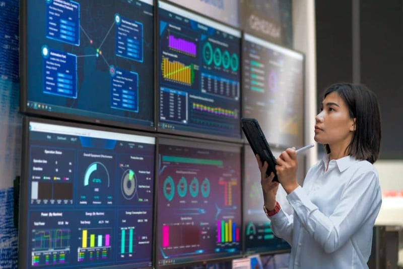 Person using tablet while reviewing wall of screens displaying digital plant data