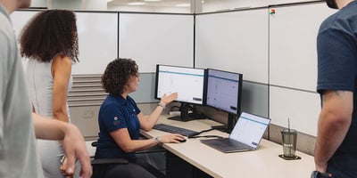 A woman presents to a group in an office desk setting.
