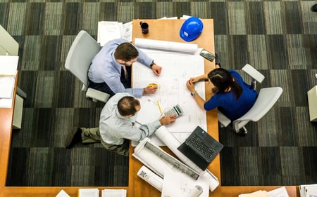 Overhead view of a meeting with engineering or architectural drafts.