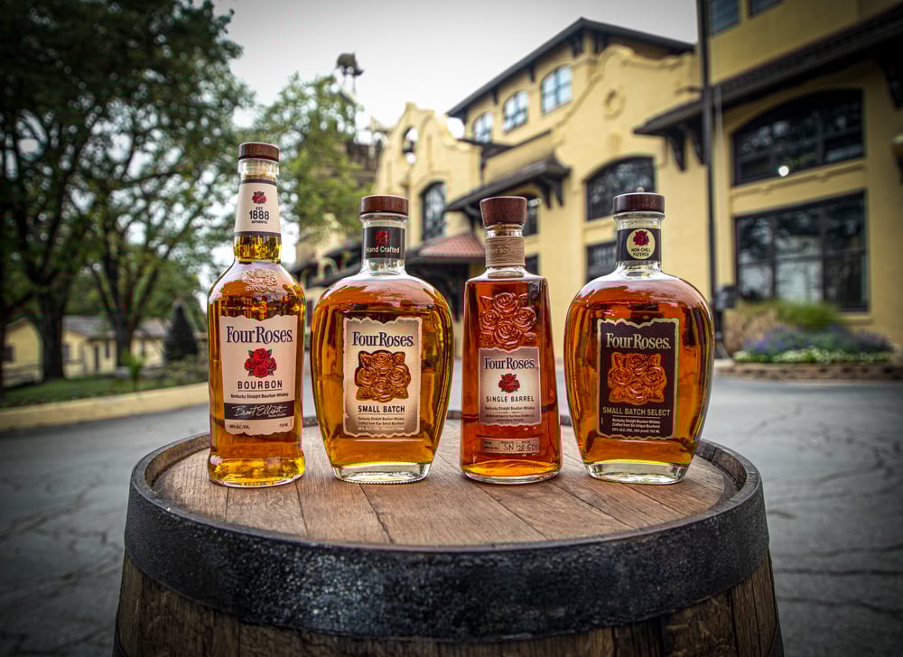 Bottles of Four Roses Bourbon in various shapes and sizes sit atop a barrel. 