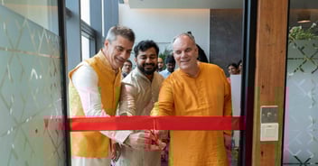 Three men cut a red ribbon while wearing traditional Indian clothes