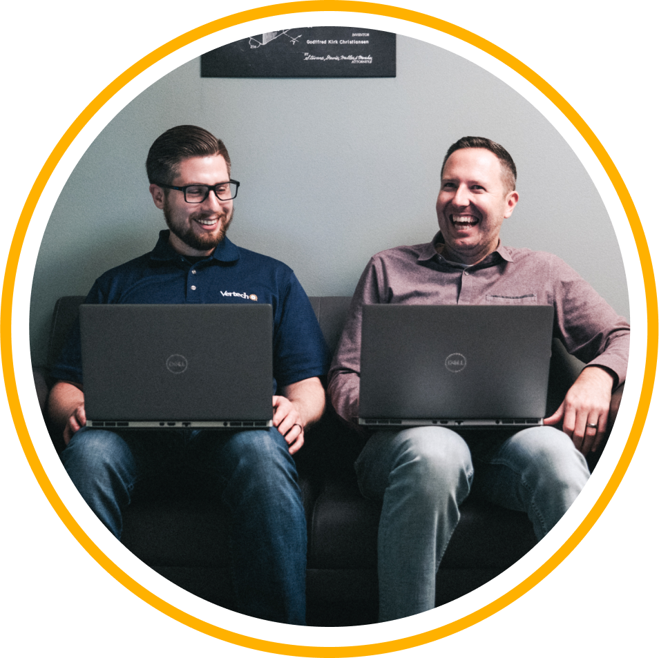 Two Vertech team members sitting next to one another, each holding laptops and smiling.