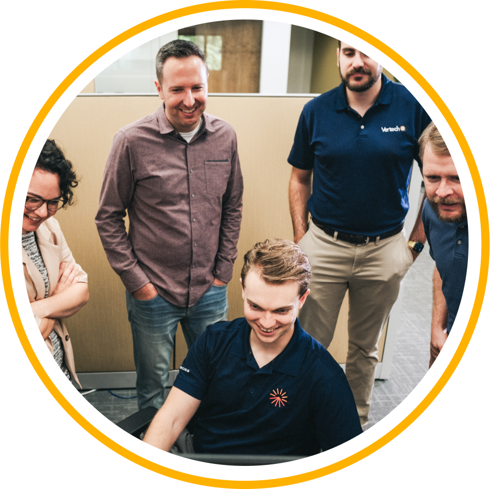 A group of five Vertech team members gather around a computer, smiling.