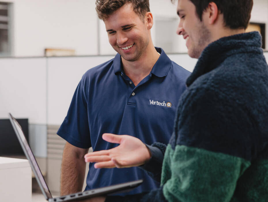 Two Vertech team members interact, smiling and looking at a laptop together. 