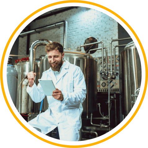 A brewery employee looks at data on a tablet, smiling and pumping his fist excitedly. 