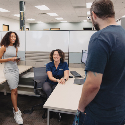 One Vertech team member sits at her desk, smiling at two other team members standing nearby.