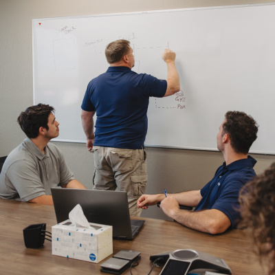A Vertech team member draws a diagram on a whiteboard in a conference room while other team members watch.