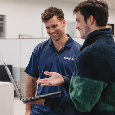 Two Vertech team members interact, smiling and looking at a laptop together. 