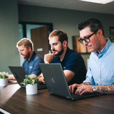 Three Vertech team members sit together at a table, each working on their own laptop.
