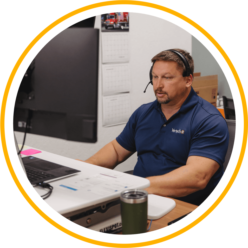 A Vertech team member wearing a phone headset sits at a desk, ready to assist.