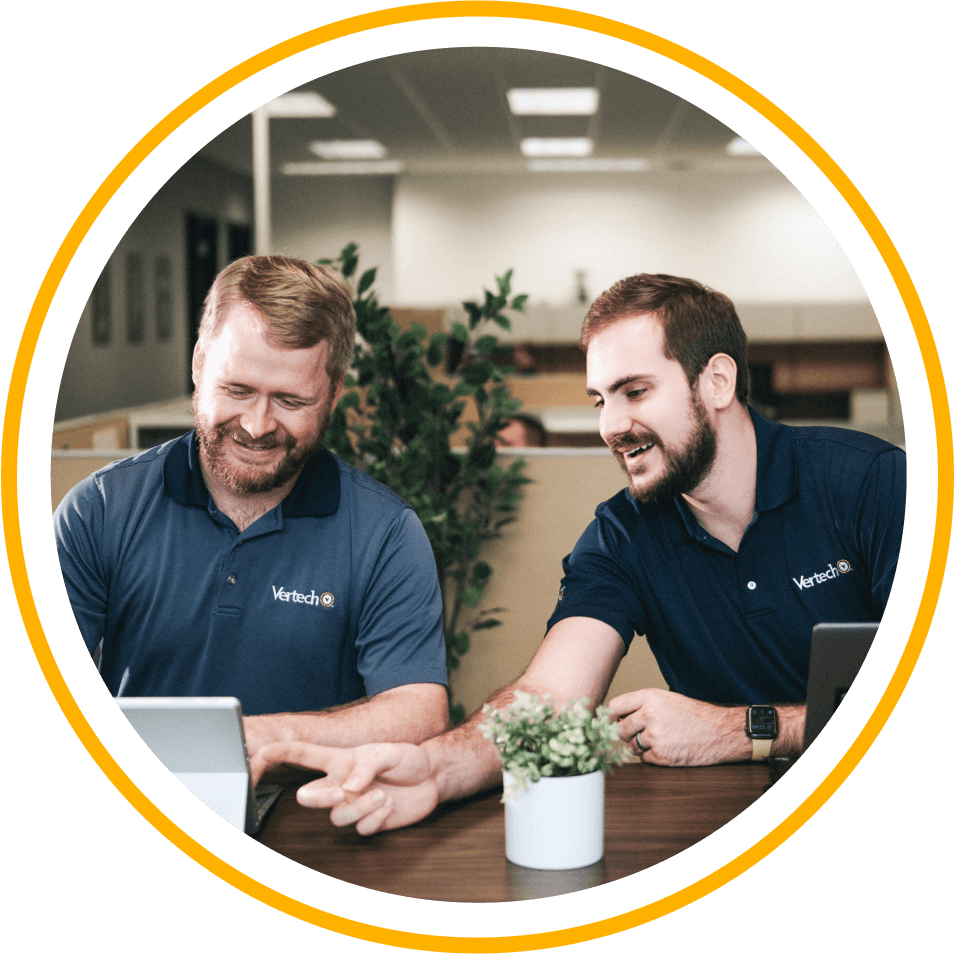 Two Vertech team members, both wearing Vertech polo shirts, look at a tablet together.