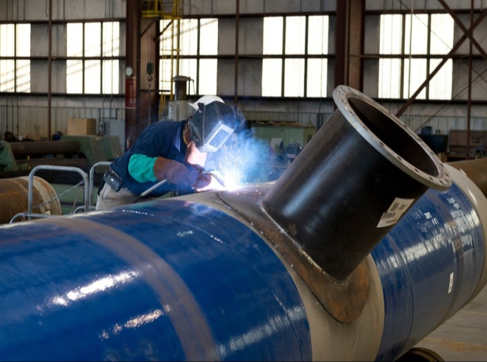 A welder works on a pipe at American SpiralWeld.