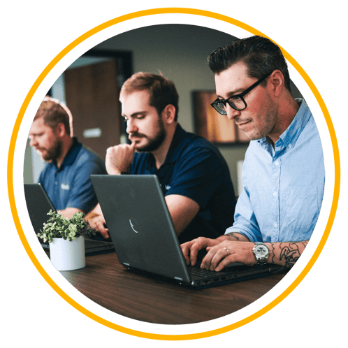 Three Vertech employees, all men, sitting at a table with laptops working together.