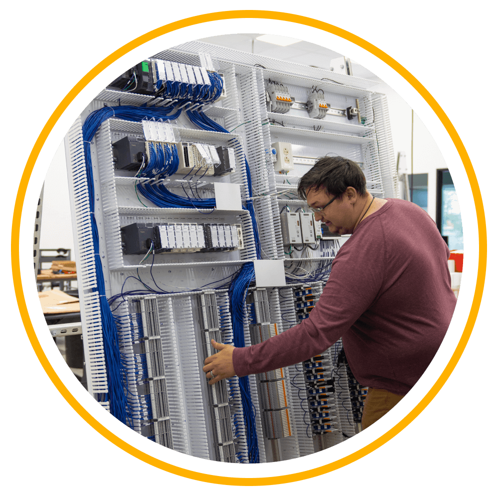 A Vertech employee, a man in a maroon shirt, standing in front of inner workings of a panel for manufacturing services.