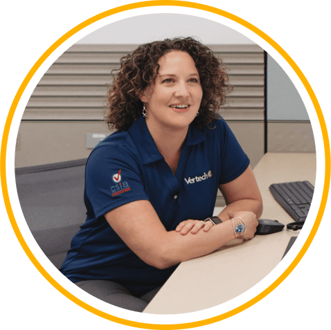 A Vertech team member wearing a blue Vertech polo shirt sits at a desk, smiling. 