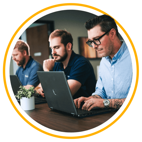 Three Vertech employees, all men, sitting at a table with laptops working together.